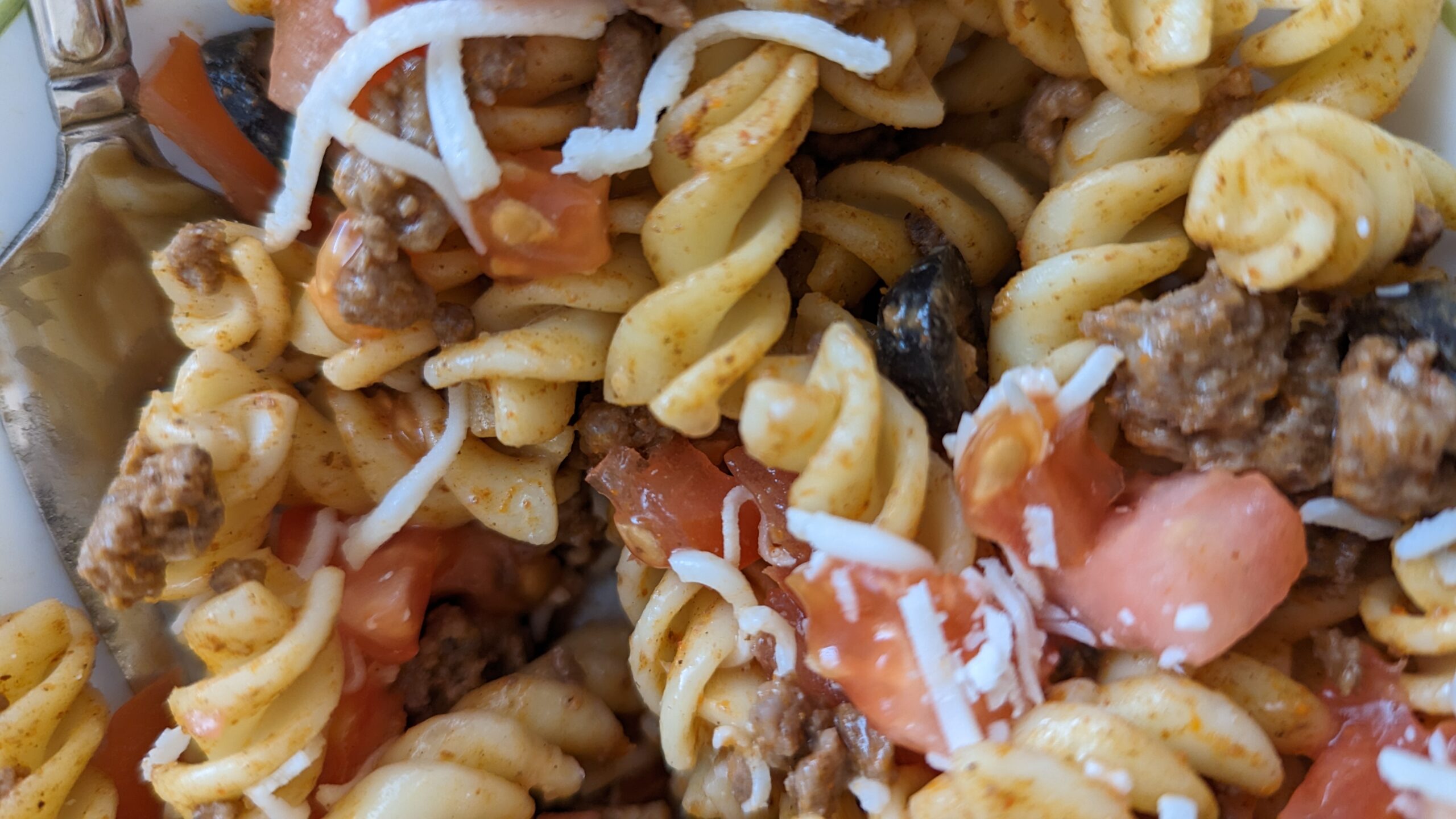 Close-up of pasta salad with noodles, tomatoes, cheese, taco meat, and olives