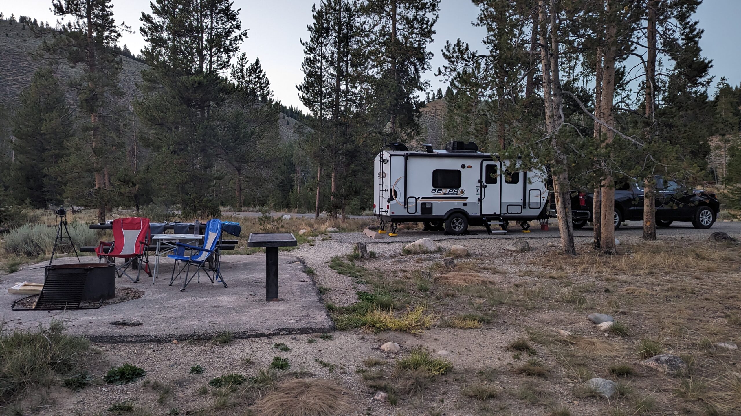 Campsite with camp chairs and a travel trailer in the background